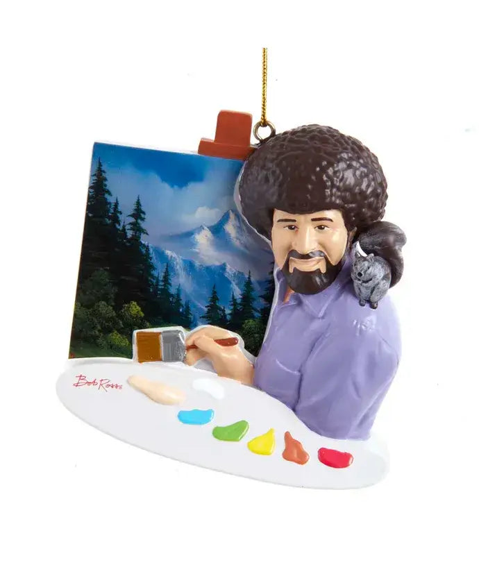 Ornament of a retro-style Bob Ross holding a paint palette and brush, sitting in front of a mountain landscape canvas with a small animal on his shoulder.