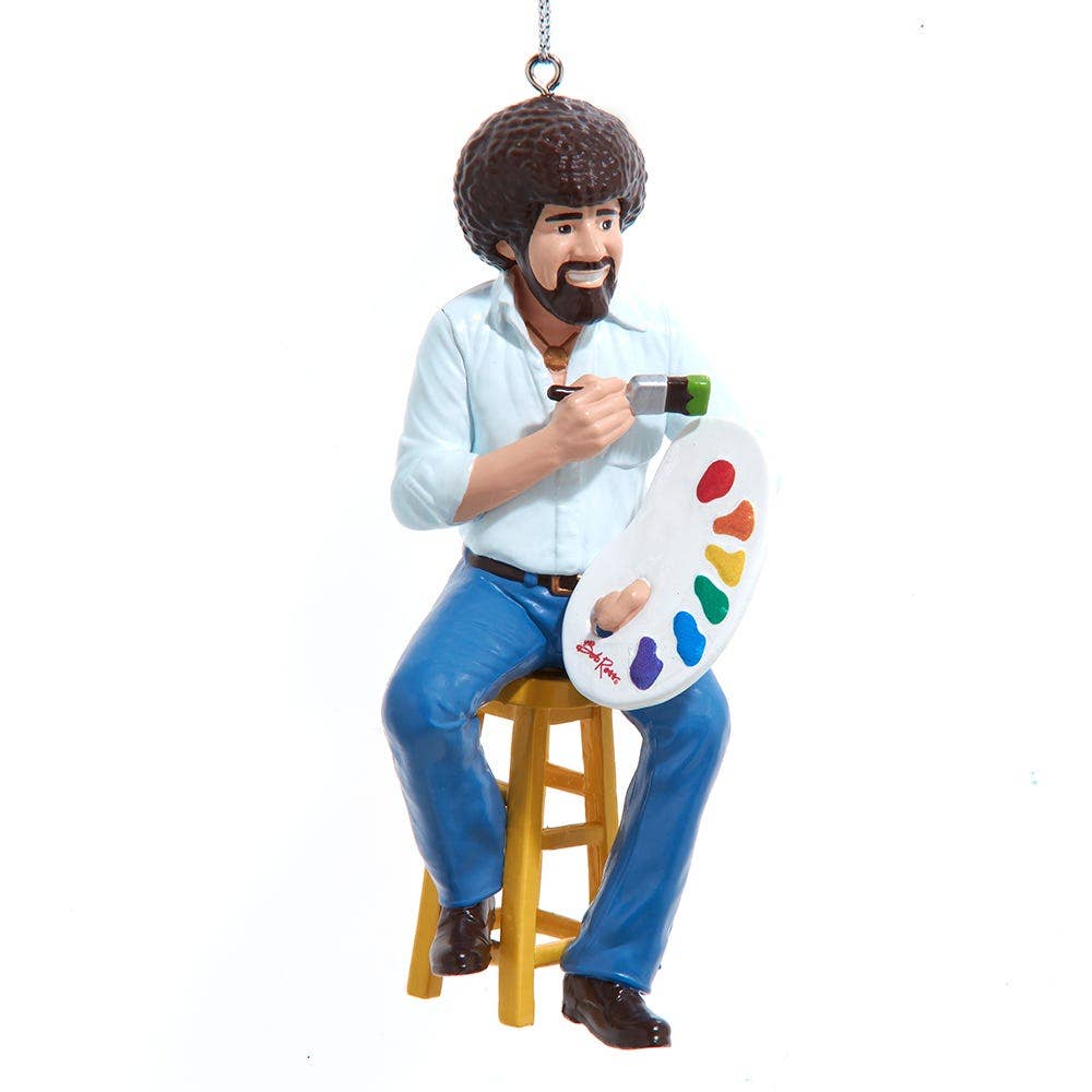 Ornament of an iconic Bob Ross TV painter sitting on a stool holding a paint palette and brush.