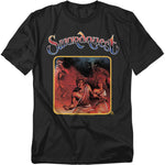 A black t-shirt featuring the Atari Swordquest artwork. The design shows a muscular hero and a woman with weapons, framed in a golden border, with a mysterious one-eyed figure and shadowy background behind them. The word “Swordquest” appears in a stylized fantasy font above the artwork.