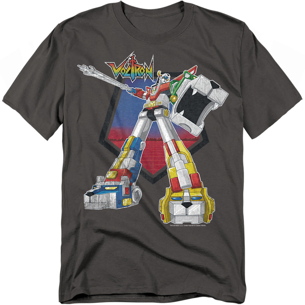 A dark gray t-shirt featuring a colorful graphic of Voltron, the legendary robot formed from five lion mechas. Voltron stands in a powerful stance with one arm raised, holding his blazing sword. The design includes bold red, blue, yellow, green, and black lion details, with the Voltron logo above the character.