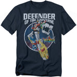 A navy blue t-shirt featuring Voltron, the giant robot made of five lion mechas, standing in a dynamic pose with one arm raised and the other extended forward. Behind him is a circular galaxy-style background. Above the design, bold white text reads “DEFENDER OF THE UNIVERSE,” with the colorful Voltron logo to the right.