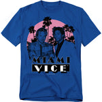 Blue t-shirt featuring Crockett and Tubbs from Miami Vice standing in front of palm trees and a neon pink sunset, with bold Miami Vice logo underneath.