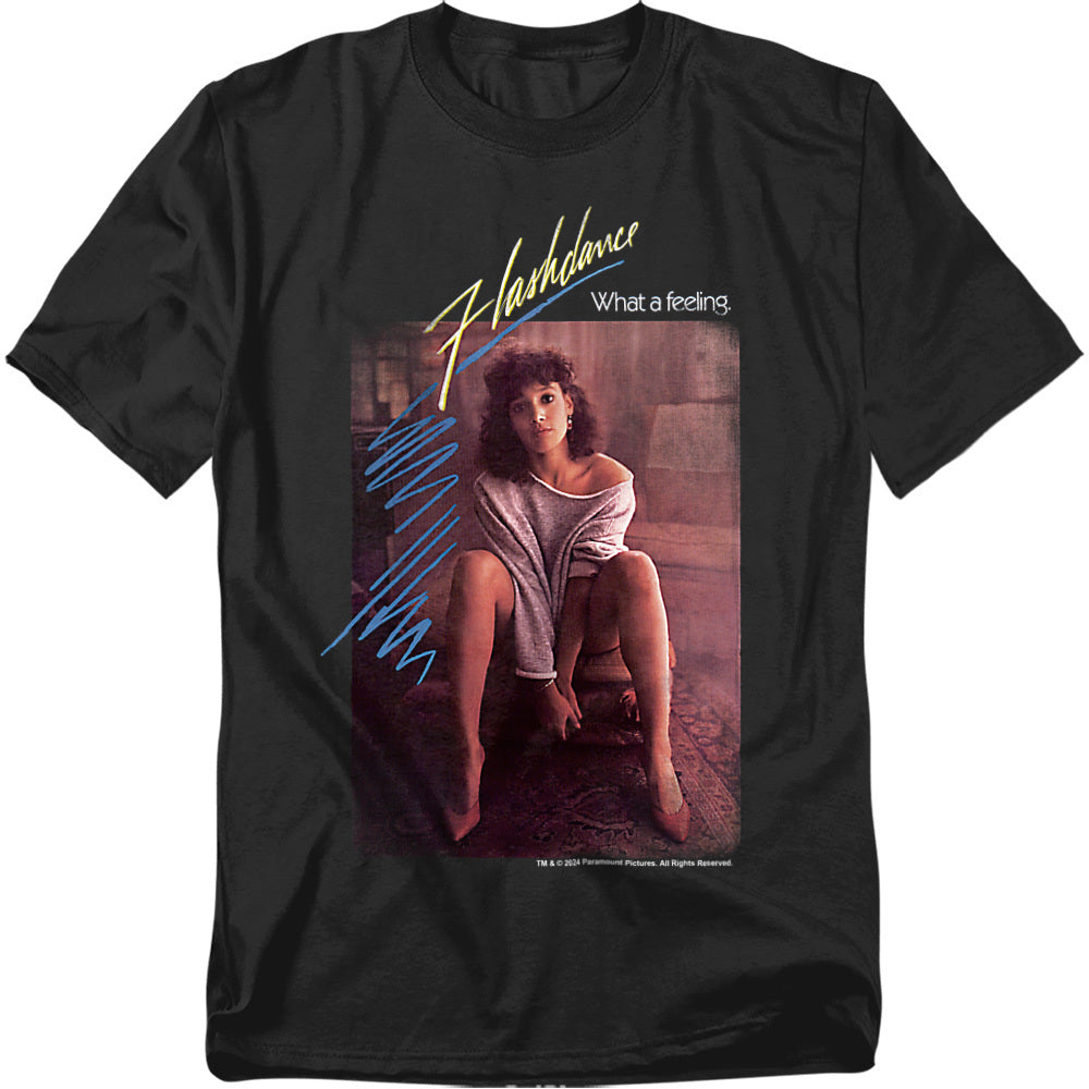 Black t-shirt with a Flashdance movie poster graphic of Jennifer Beals sitting in her off-the-shoulder sweatshirt with “Flashdance What a Feeling” text.