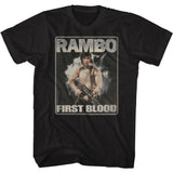 Black vintage-style t-shirt featuring the classic Rambo: First Blood movie poster art, with John Rambo holding a machine gun and standing against a smoky, action-filled backdrop.