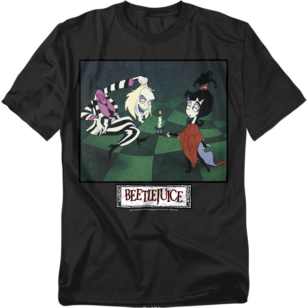 A black t-shirt featuring a colorful print from the Beetlejuice animated series. The artwork shows Beetlejuice crouched playfully in his black-and-white striped suit, grinning at Lydia Deetz. Lydia, wearing her red spiderweb poncho, holds a lit candle while giving a sly smile. The Beetlejuice logo appears below the image in a distressed white box with red lettering.
