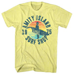 Pale yellow Jaws T-Shirt featuring a surfer silhouette, retro sunset artwork, and Amity Island Surf Shop 1975 graphic
