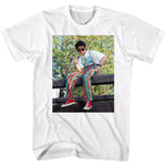 White T-shirt featuring a full-color photo of Screech Powers from Saved by the Bell wearing colorful patterned pants, red sneakers, and sunglasses while sitting on a wooden fence.